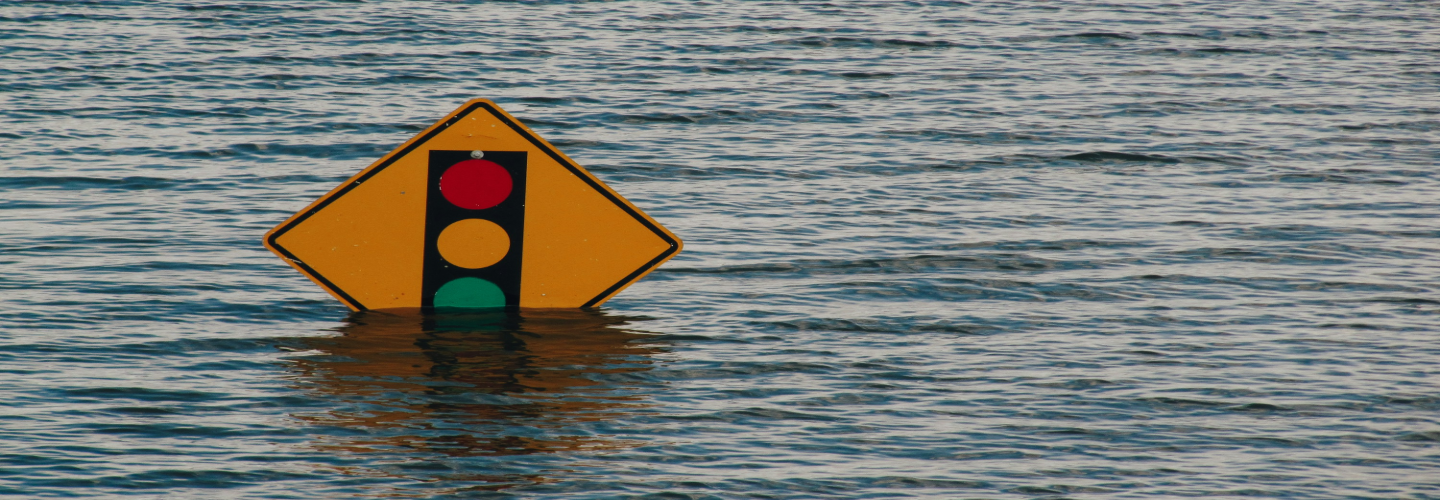 A partially submerged traffic signal warning sign in floodwater, symbolizing the impact of rising water levels due to climate change and extreme weather events.
