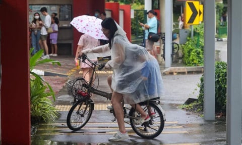 A girl cycling in rain with a raincoat over her