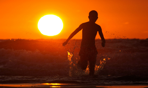 Silhouette of a person running through ocean waves against a vibrant hot sun