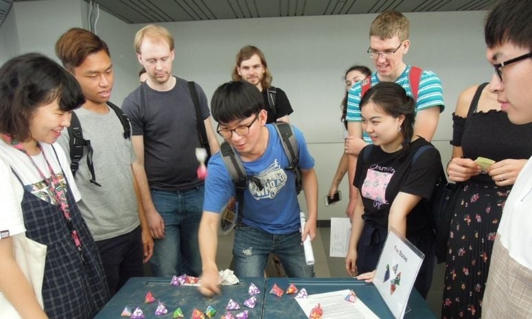 A student playing five stones while a group of students look on.