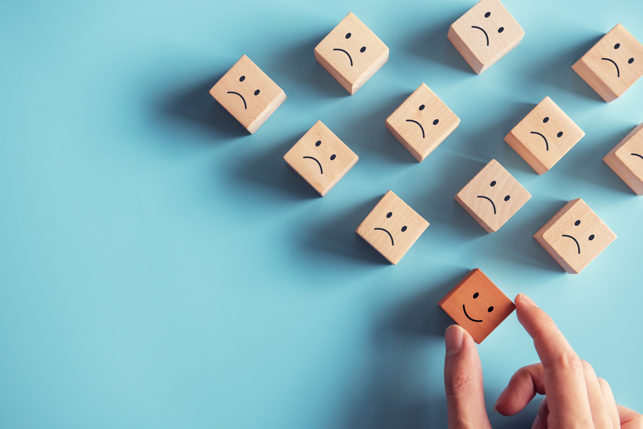 Positive attitude and happy concept. Hand choose wood cube a smiley face surrounded sad emotion