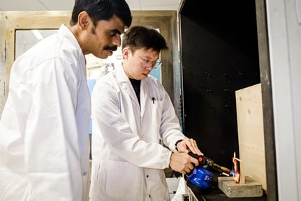 Associate Professor Aravind Dasari with PhD student Dean Seah from NTU fire testing a piece of timber that has an invisible coating which makes it 'fireproof'
