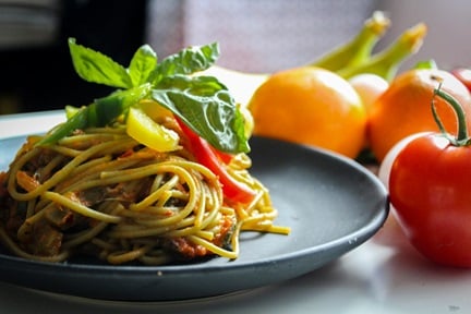 Pasta with vegetable dish on gray plate beside tomato on white table