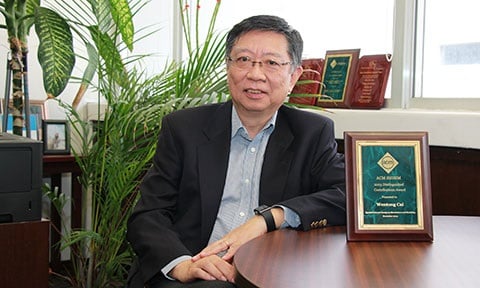 Photo of Prof Cai sitting in his office next to a plaque on the table.