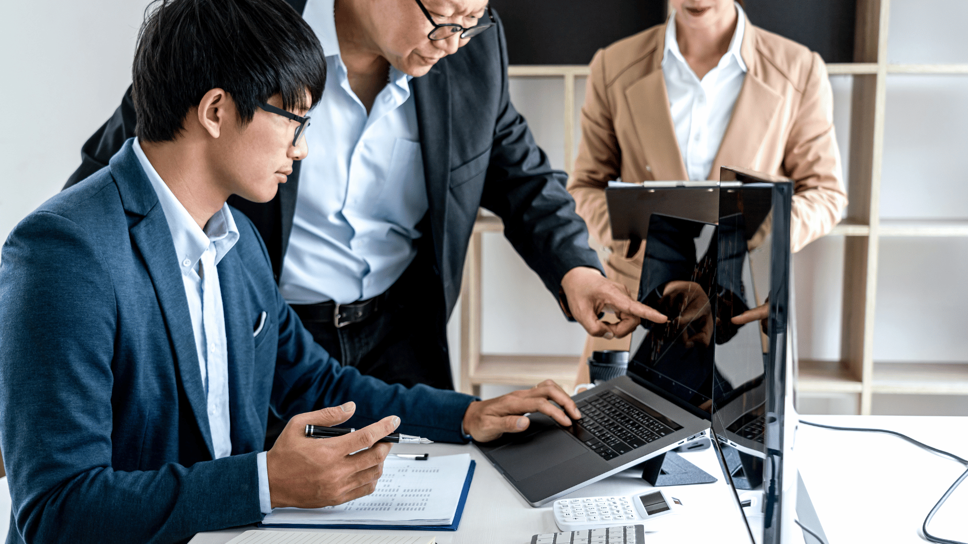 Team of investors working together and analysing stock data graphs on a laptop screen