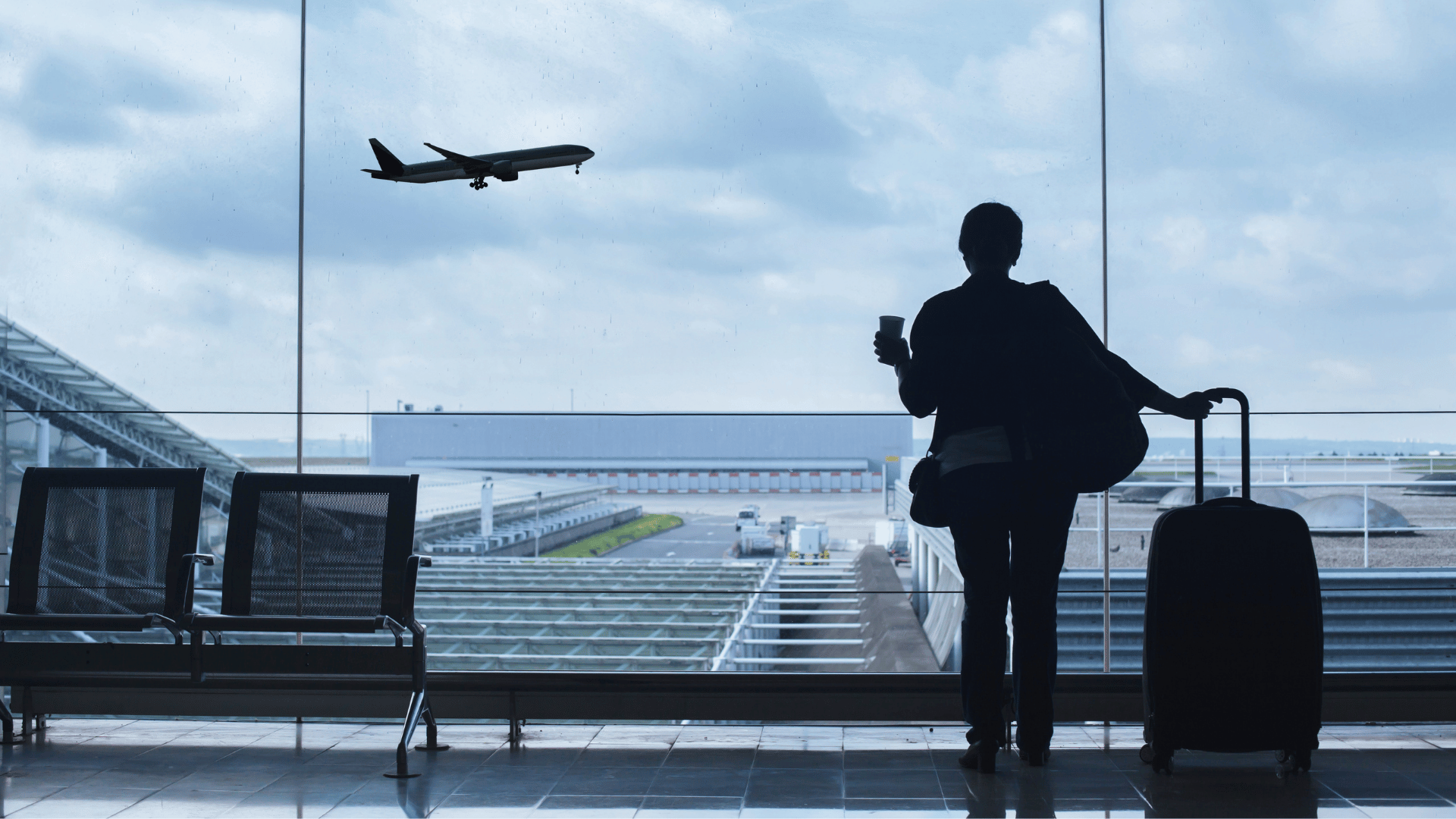 A traveller with a luggage looking an airplane taking off