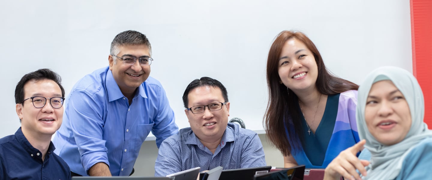 3 Male Teachers And 2 Female Teachers All In Blue Smiling In Classroom Looking Forward