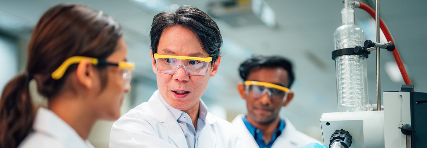 3 Scientists In Yellow Goggles In A Science Lab And Lab Coats