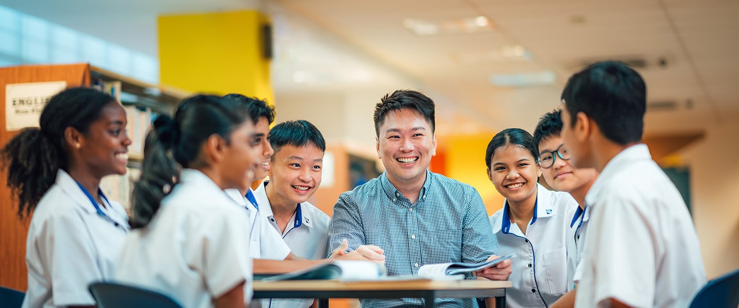 Male Teacher with Group of 7 Secondary Students in Uniform in the Library