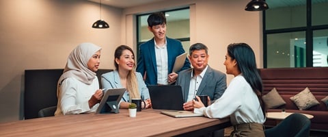 Older Male Teacher In A Grey Blazer With Group Of 4 Young Adult Students In Meeting Room