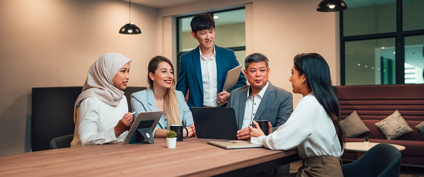 Older Male Teacher in Grey Blazer iPad with Group of 4 young students in casual business wear
