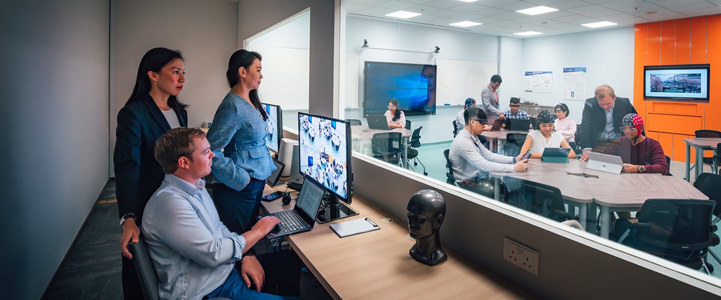 SoLEC Classroom with Caucasian Man Looking At Computer Screen Monitoring Students On The Inside Of Classroom Behind The Glass Window