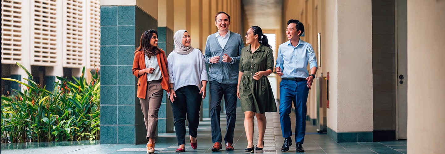 Tall Male Teacher In Grey Cardigan Walking Along NIE Campus With 4 Other Young Adult Students In Casual Businesswear