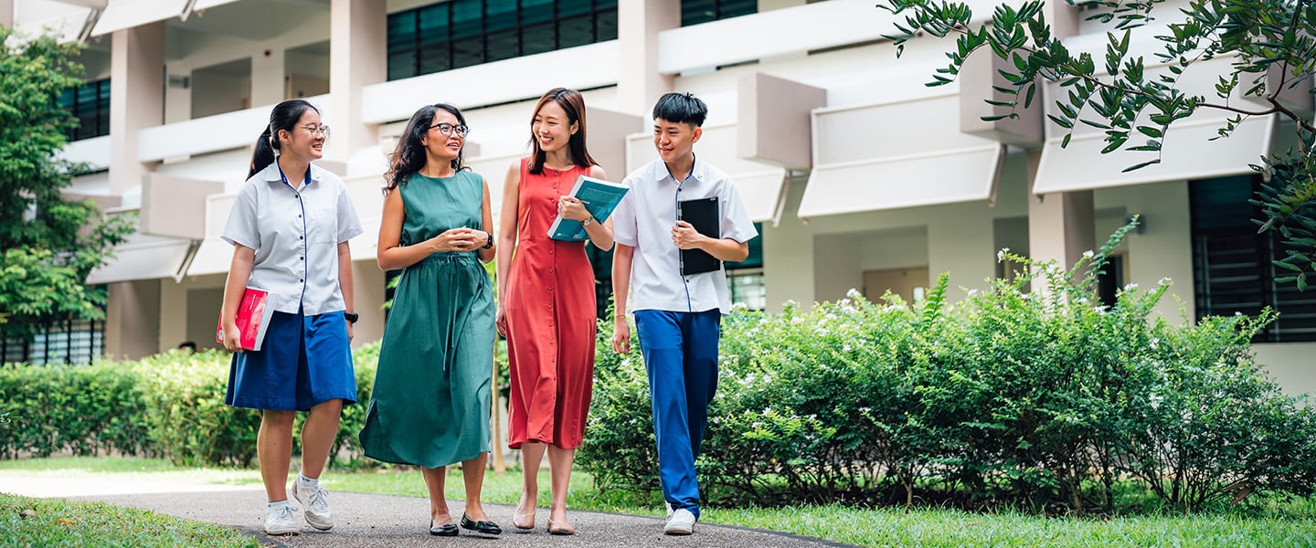 Tanned Female Teacher in Green Dress and Chinese Girl in Red Dress Walking with 2 Secondary School Students