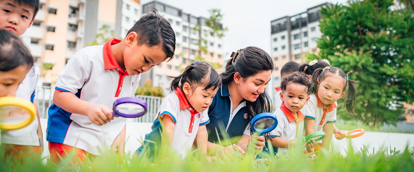 Toy Magnifying Glass Kindergarten Students And Teacher Outside On A Grassy Field Looking Down Inquisitively