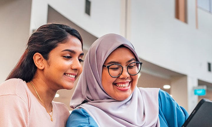 iPad Malay Student Wearing Tudung with Indian Girl in Pink Top Looking at iPad in NIE Library Closeup (720x432px)