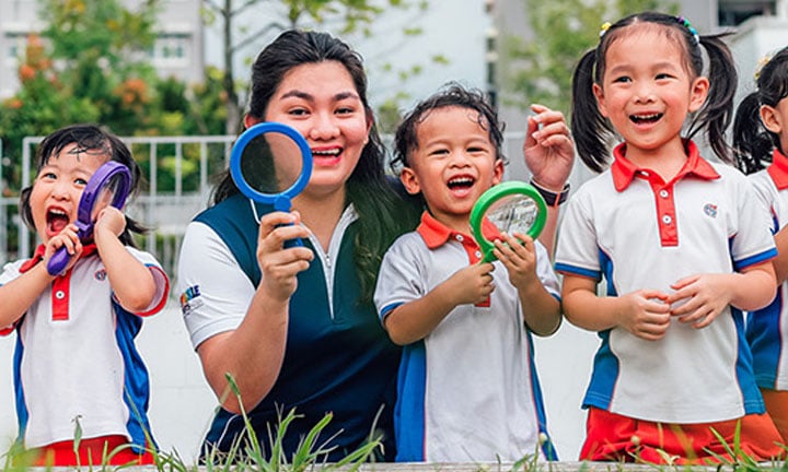 Toy Magnifying Glass Kindergarten Students And Teacher Outside On A Grassy Field Looking Straight Ahead All Smiles Closeup (720x432px)