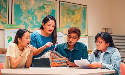 A Volcano Model Discussed by Group of 4 young students teacher blue dress wideshot 480x288px)