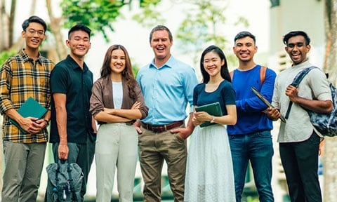 Smiling Group of 7 Young Adult Teachers Chinese Boy Yellow Gingham Plaid Shirt Caucasian Man Light Blue Shirt Closeup