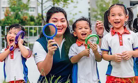 Toy Magnifying Glass Kindergarten Students And Teacher Outside On A Grassy Field Looking Straight Ahead All Smiles Closeup (480x288px)